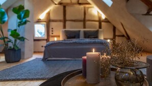 Une chambre mansardée chaleureuse, avec un lit, deux bougies et un vase de fleurs séchées posé sur un plateau.
