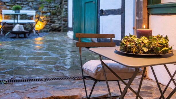 Un espace extérieur aménagé avec une table et des chaises, une bougie et un chemin de pierres menant à un bâtiment doté d’une porte verte.
