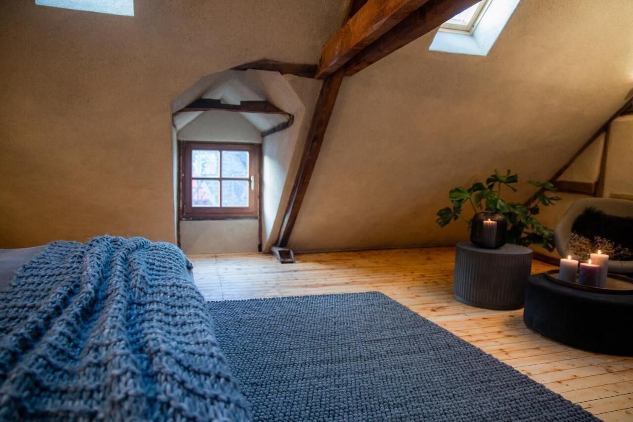 Ein gemütliches Schlafzimmer im Dachgeschoss mit schrägen Wänden, einem Fenster, einem Kamin und einer gemütlichen Sitzecke mit Kerzen.