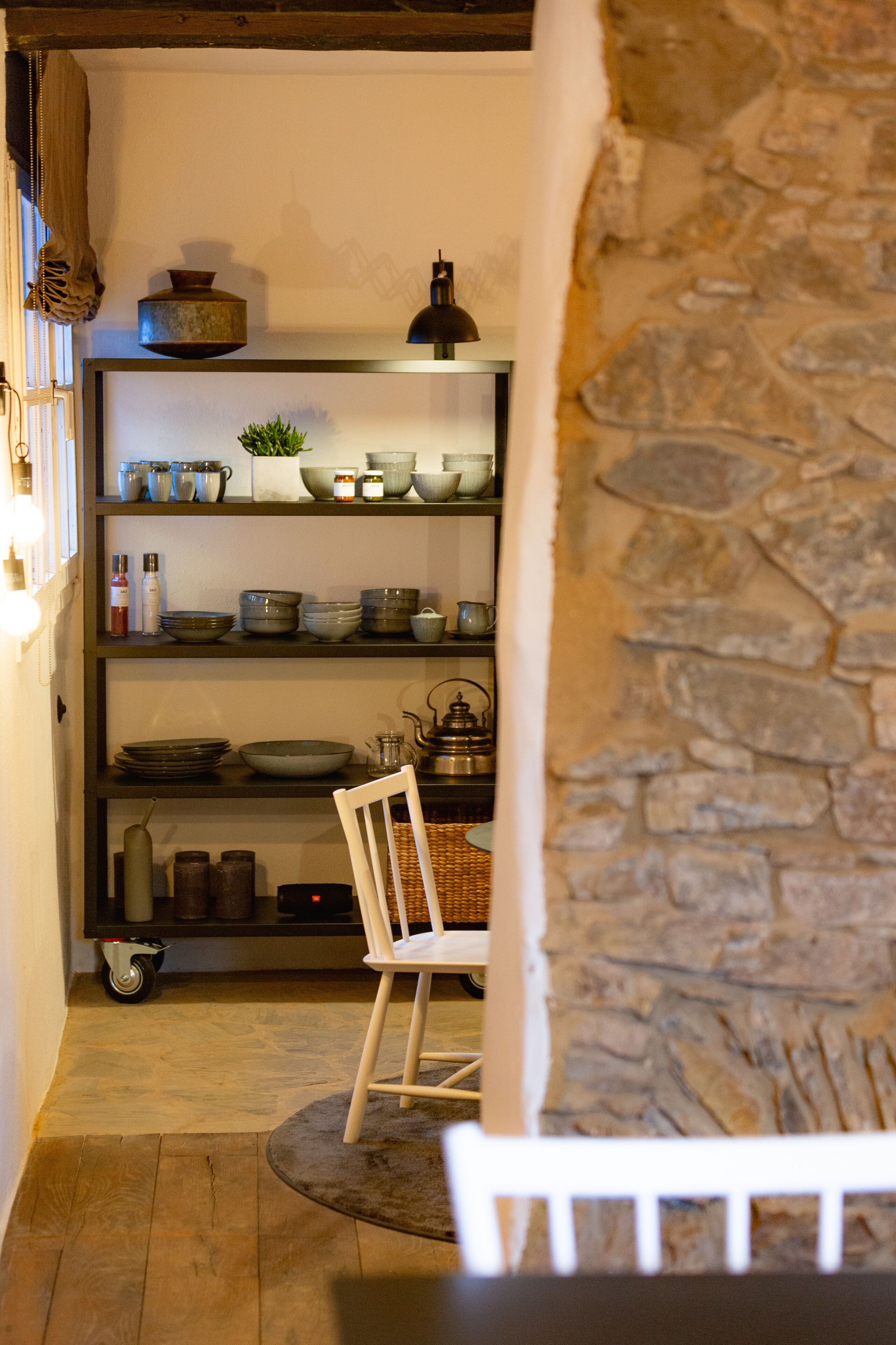 Ein rustikales Interieur mit Steinwand, Holzboden und einer Ablage mit verschiedenen Küchengegenständen.