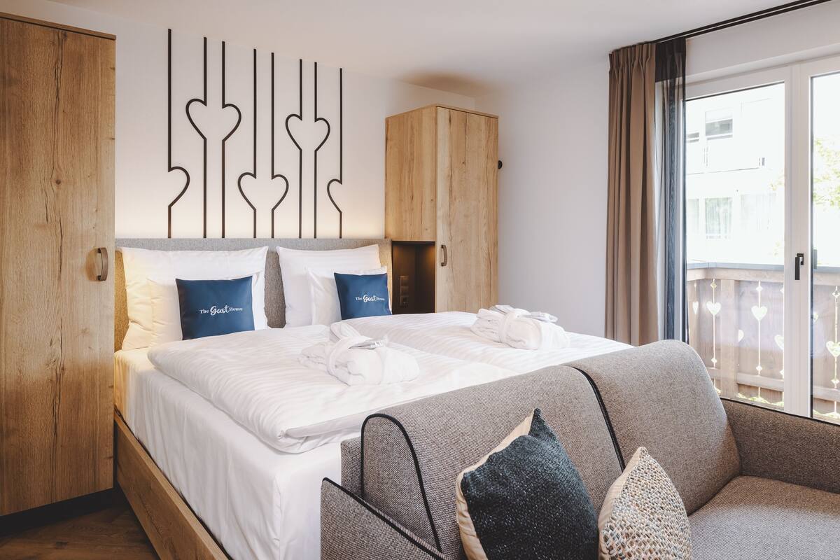 Una habitación de hotel con una cama, un armario de madera, un sofá gris y un adorno en la pared.