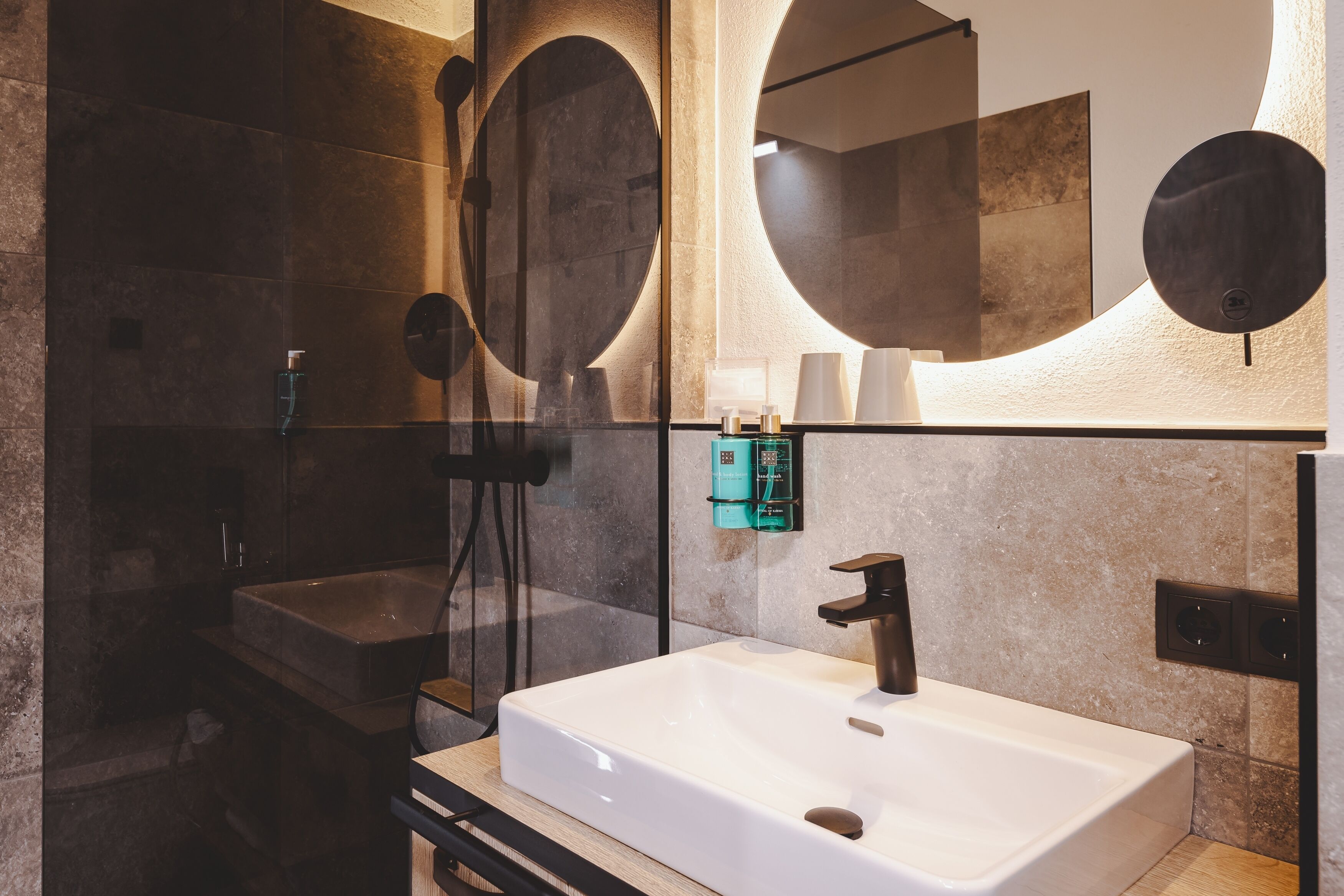 A modern bathroom with a large mirror, a sink, and a shower.