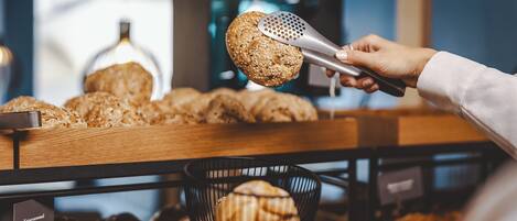 Una persona eligiendo un bollo de pan de una vitrina de panadería.