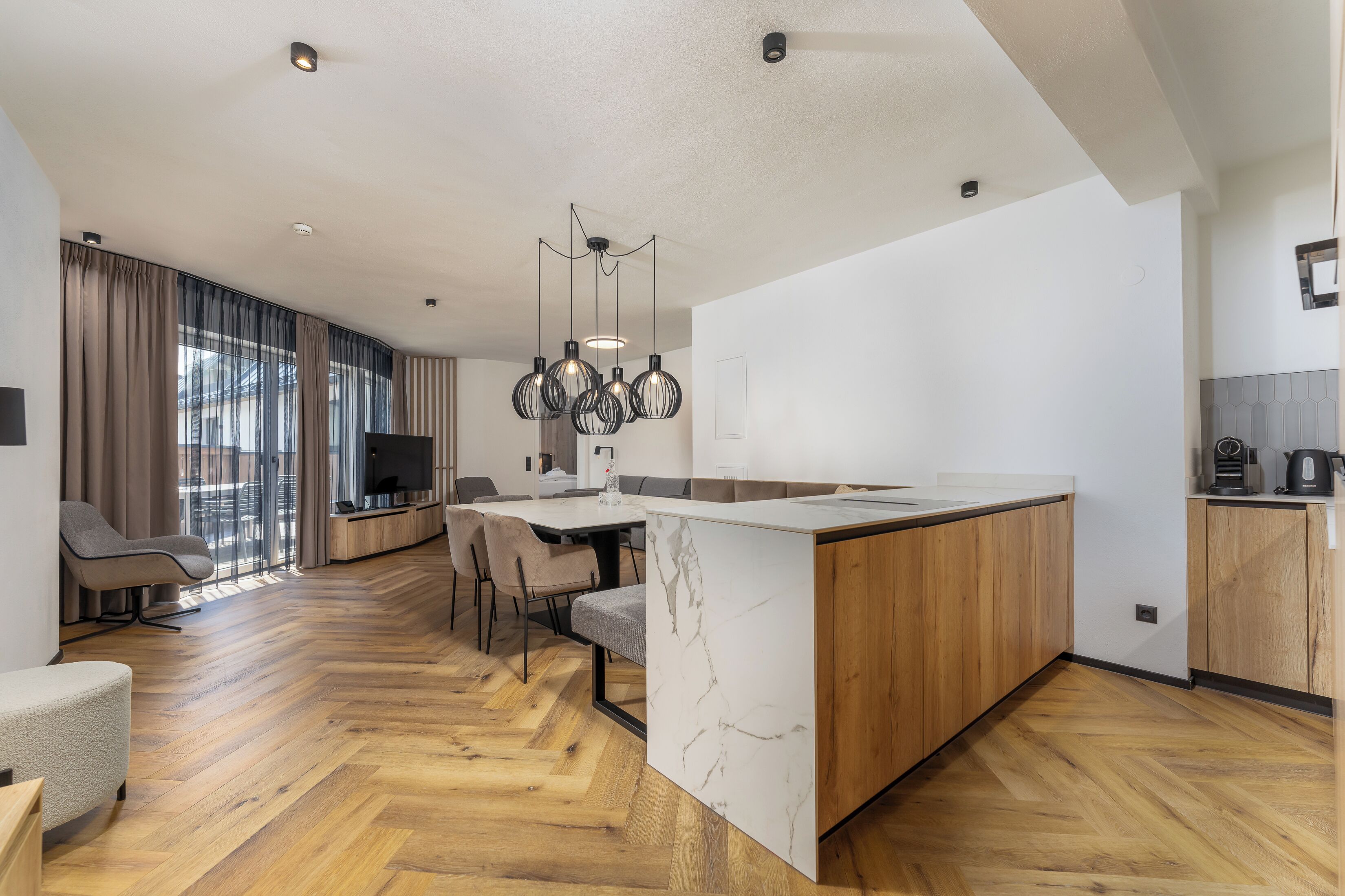 A modern kitchen with a marble island, wooden cabinets, and a dining area with chairs and a table.