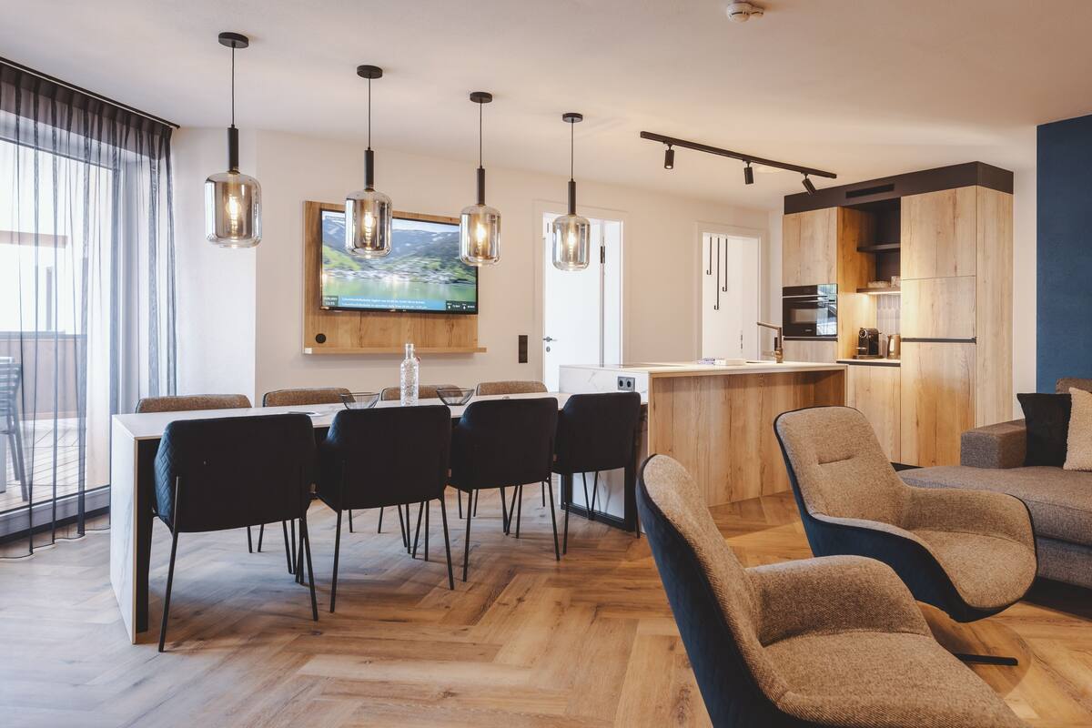 Una cocina moderna con armarios de madera, un comedor con una mesa grande y sillas, y una sala de estar con sofás.