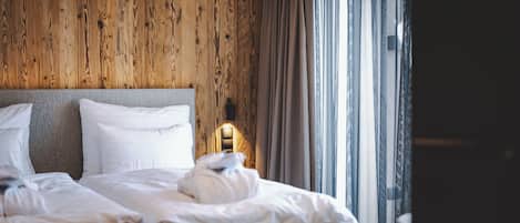 A hotel room with a wooden wall, a large bed with white linens, and a nightstand with a lamp.