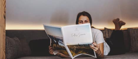 En person läser en bok med titeln ”Oändlig sommar” i ett modernt vardagsrum med en soffa, ett bord och en unik svart hänglampa.