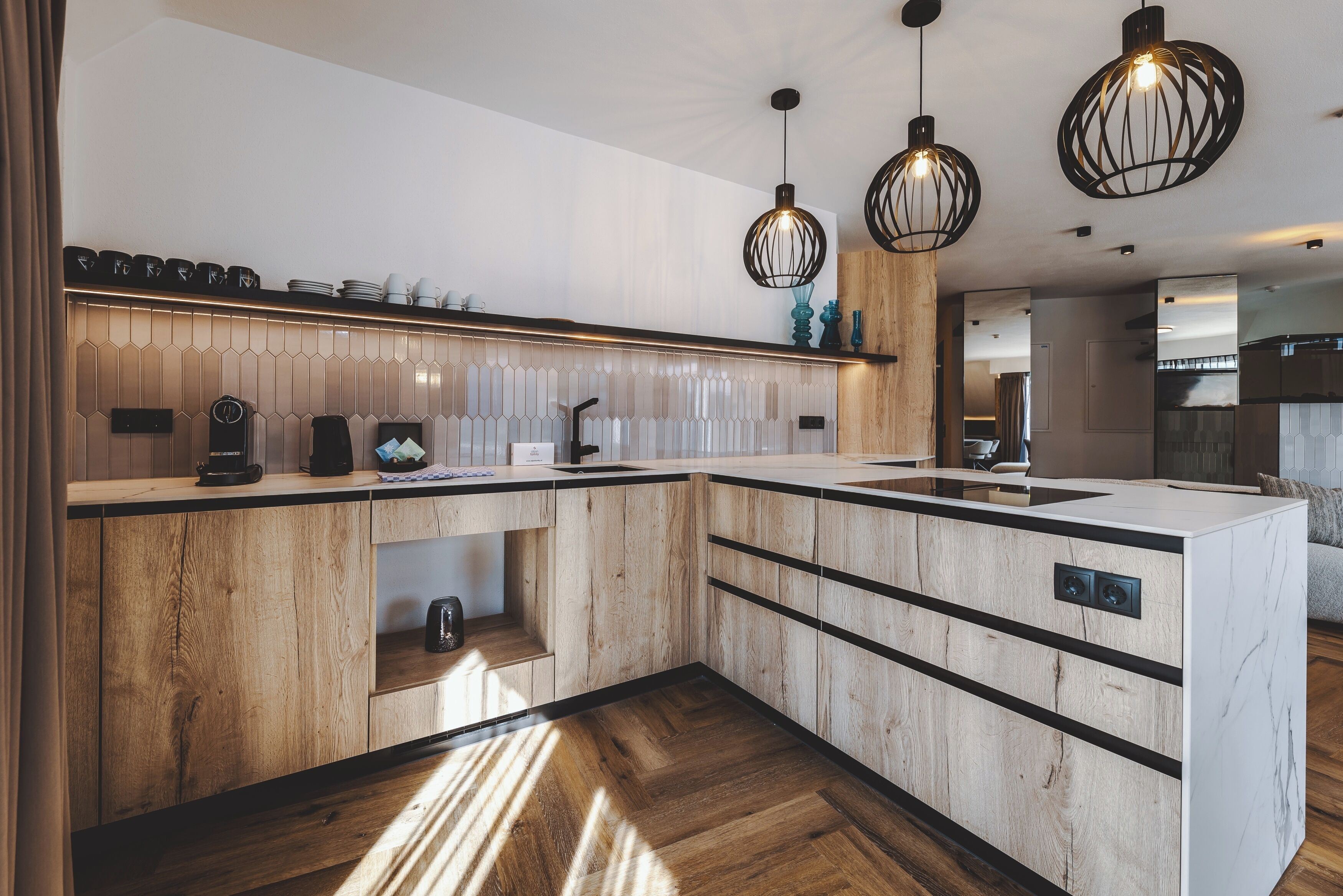 Een moderne keuken met houten kastjes, een marmeren aanrechtblad en hanglampen.
