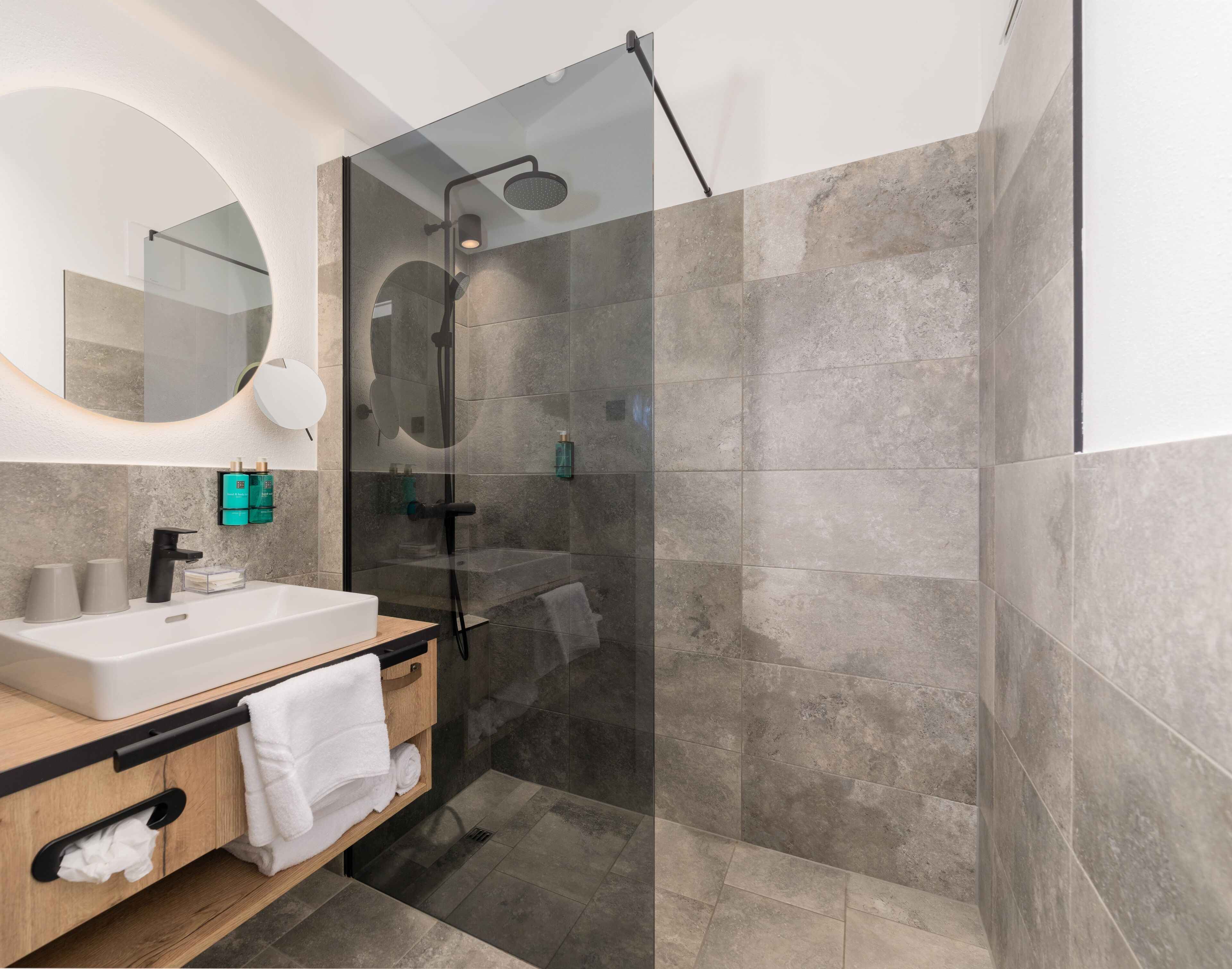 A modern bathroom with a glass-enclosed shower, a white sink, and a wooden vanity.