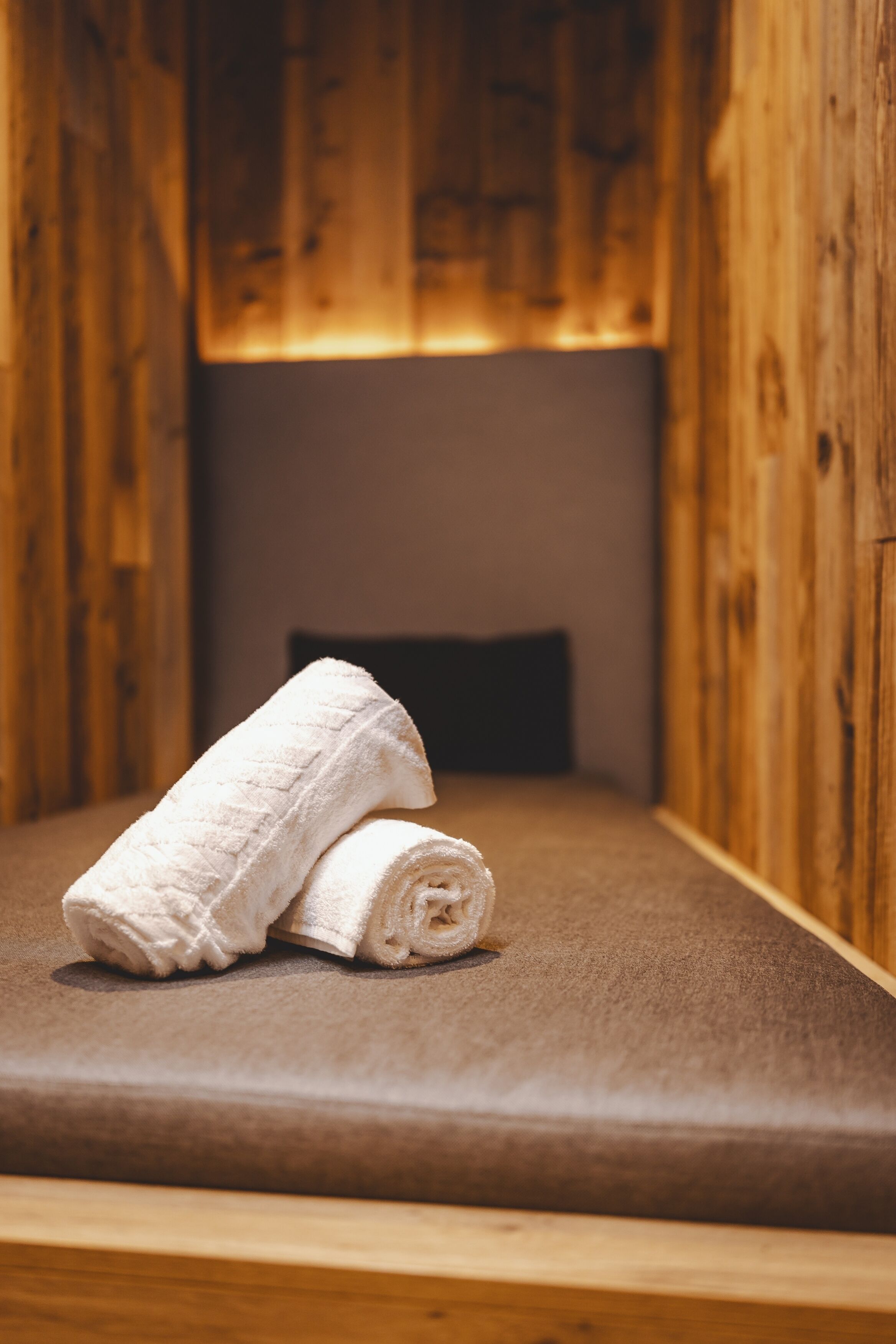 A wooden room with a bed, a pillow, and a rolled-up towel.