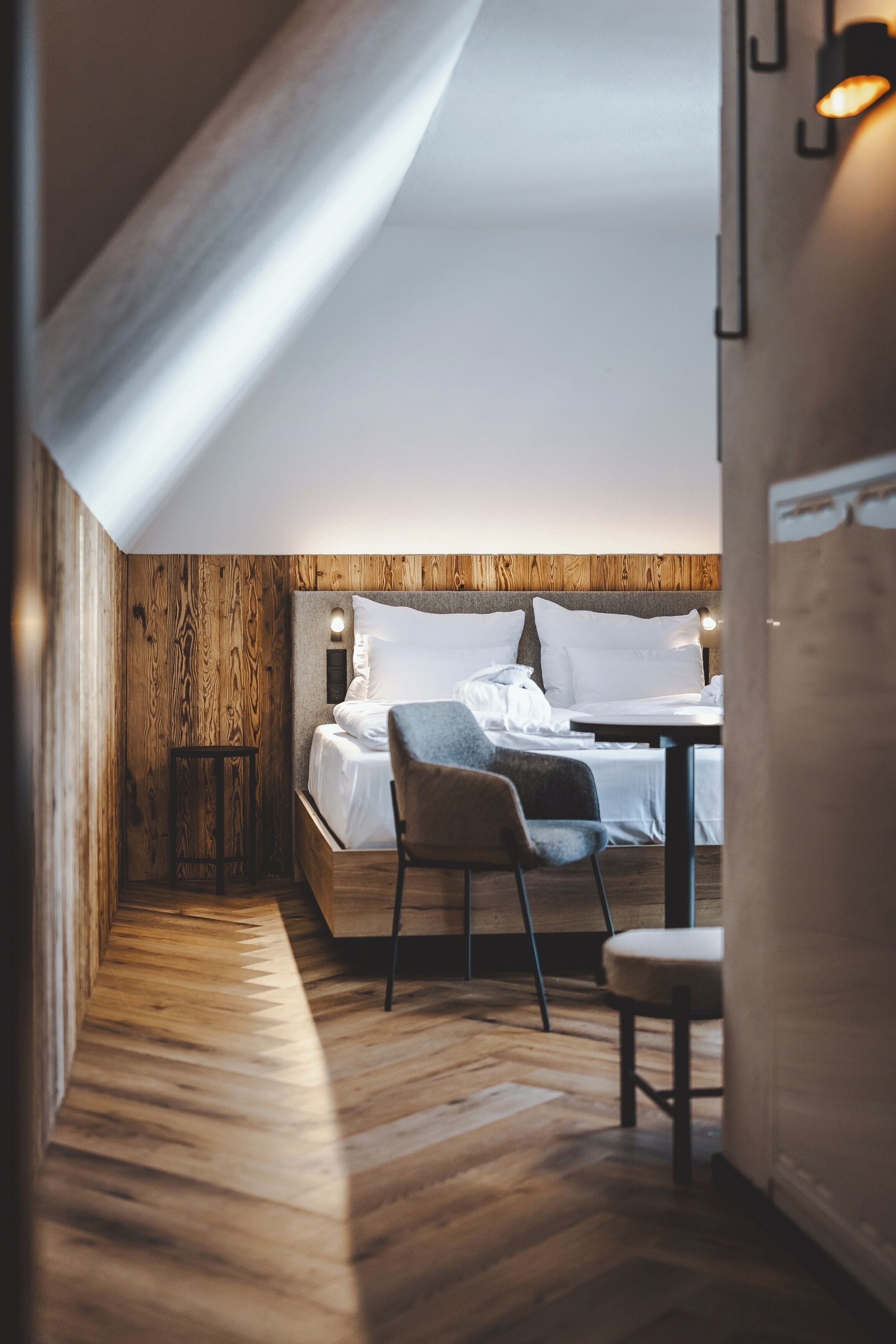 A cozy bedroom with a wooden ceiling, a bed with white linens, a small table, and a chair.