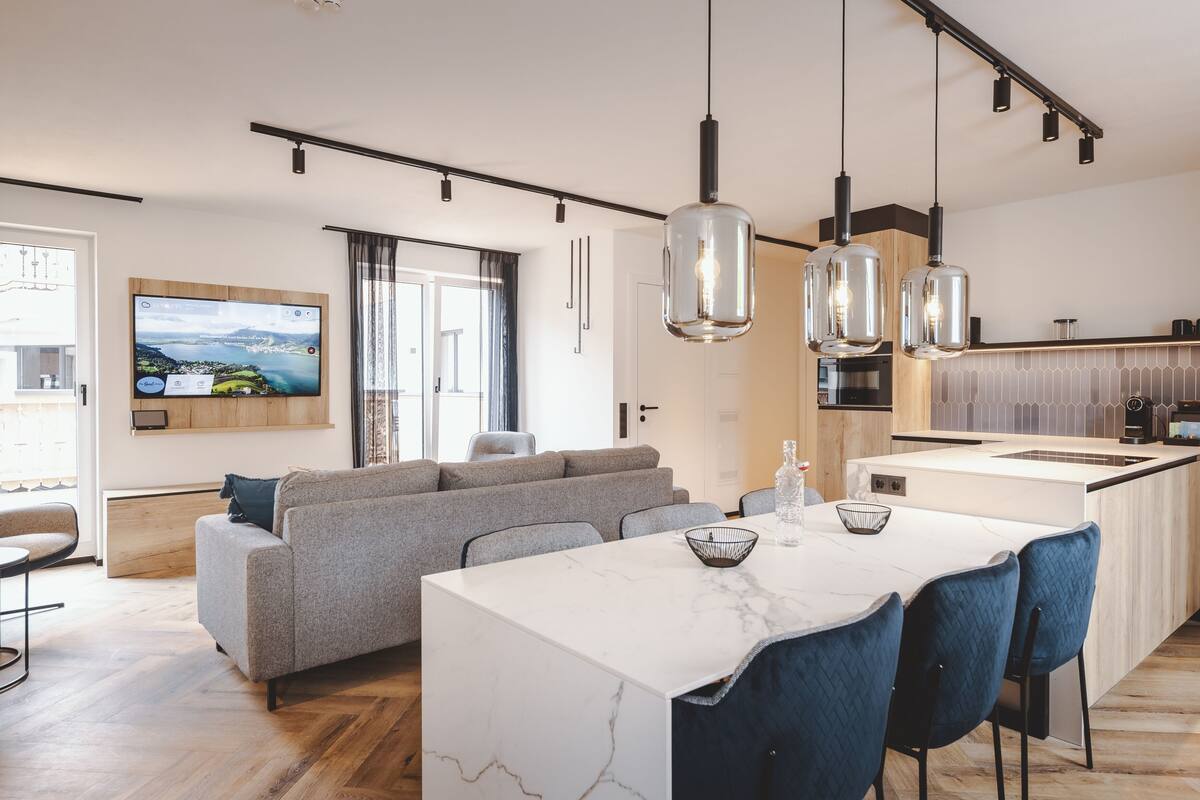 Una cocina moderna con una isla de mármol, luces colgantes y un comedor con sillas azules.