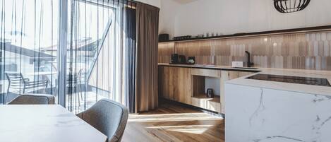 Una cucina moderna con un piano di lavoro in legno, un'isola in marmo e vista sull'area salotto esterna.