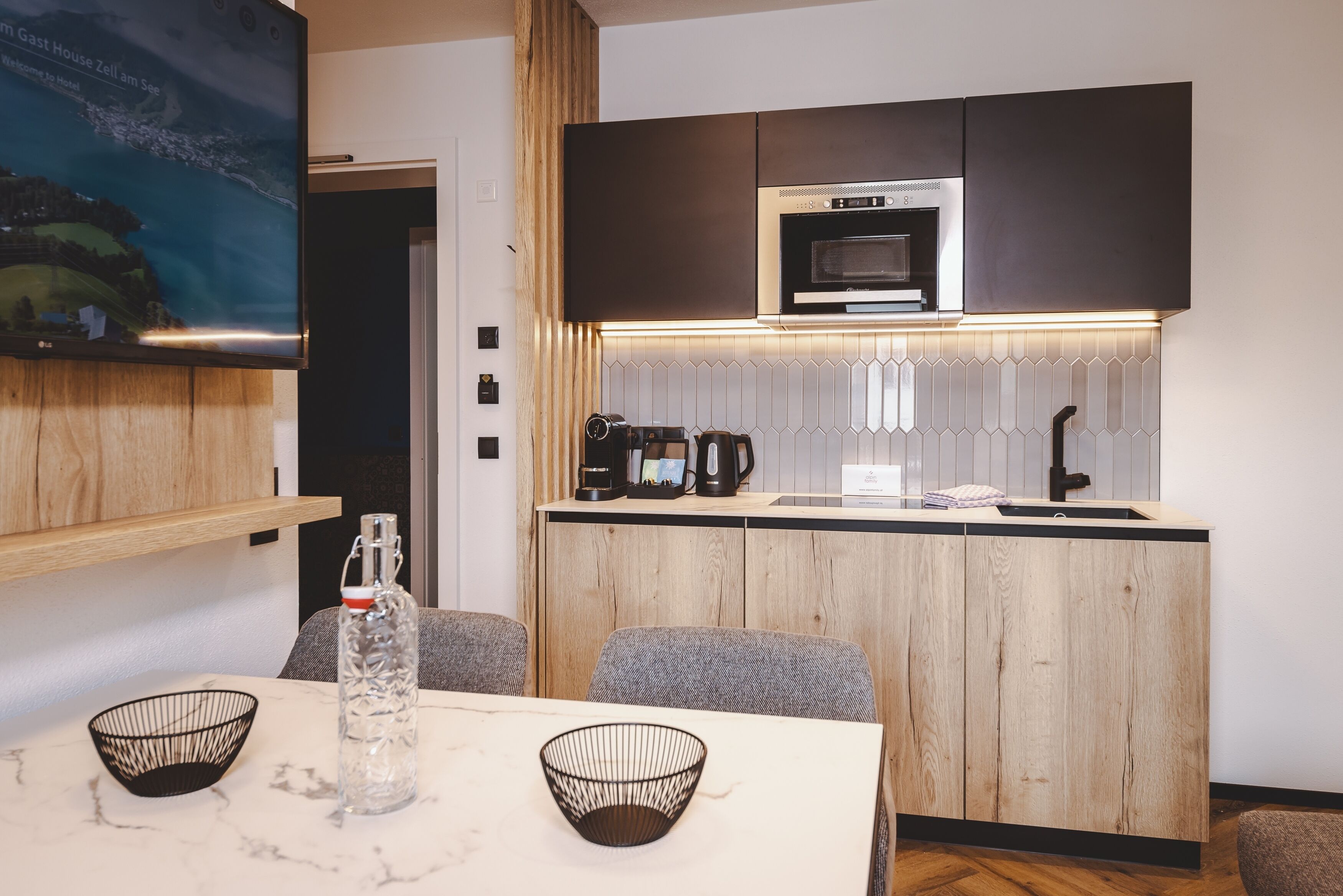 Een moderne keuken met een ingebouwde magnetron en koffiezetapparaat, een houten aanrecht en een eethoek met een tafel en stoelen.