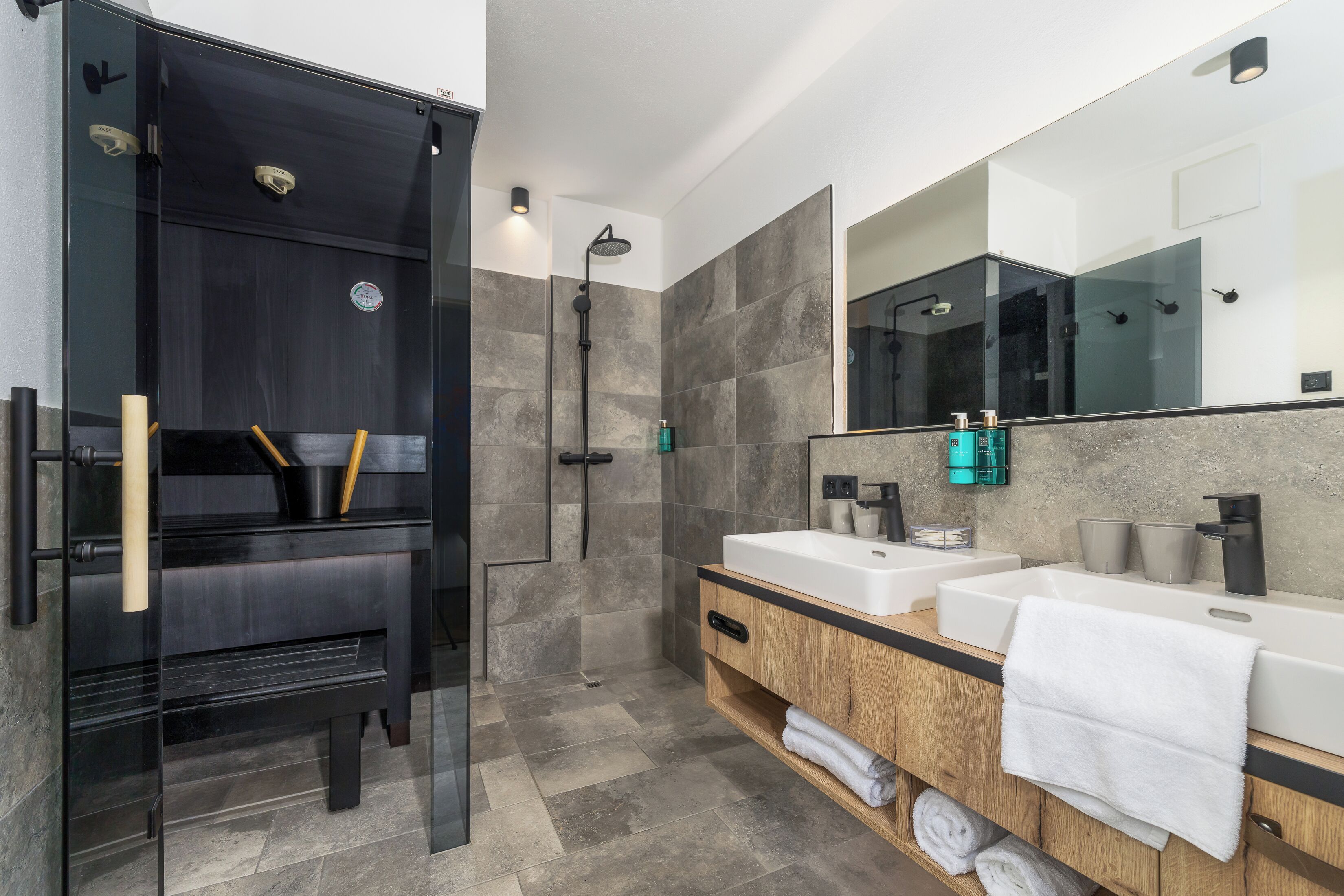 Un baño moderno con cabina de ducha de vidrio, tocador de madera con dos lavamanos y un espejo grande.