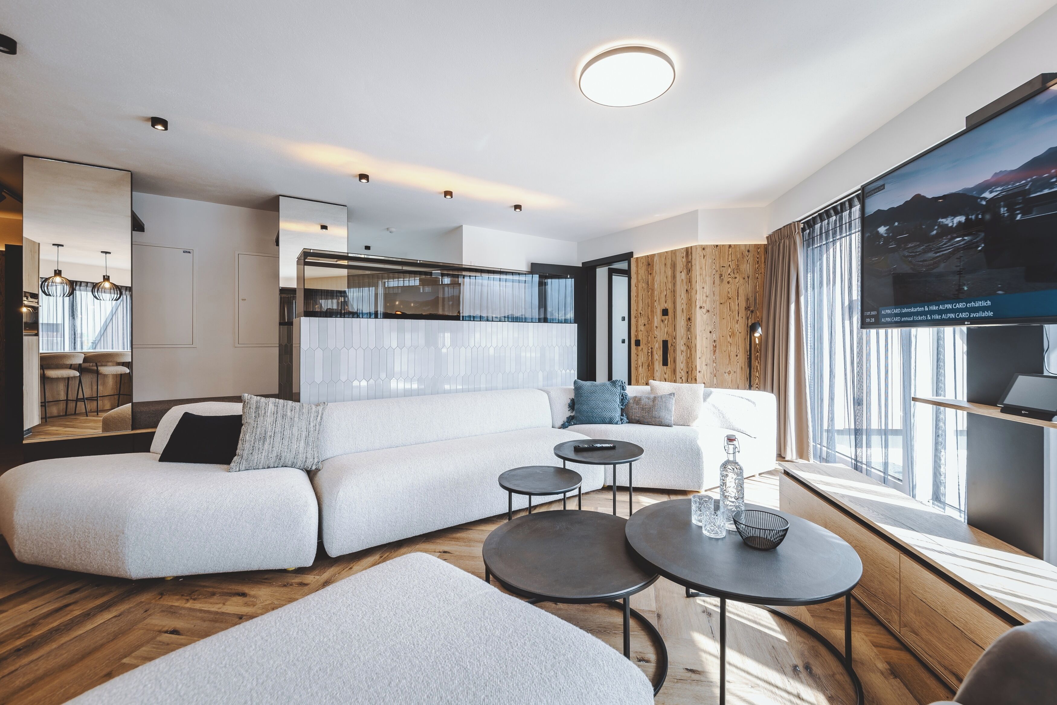 Ein modernes Wohnzimmer mit Ecksofa, runden Couchtischen und einem großen Fenster mit Aussicht.