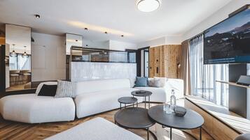 Ein modernes Wohnzimmer mit Ecksofa, runden Couchtischen und einem großen Fenster mit Aussicht.