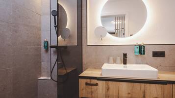 Un baño moderno con tocador de madera, un espejo grande con iluminación circular y una zona de ducha.