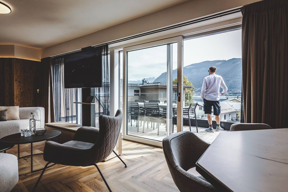 Habitación de hotel moderna con un amplio ventanal corredero que da a un balcón con vistas a la montaña.