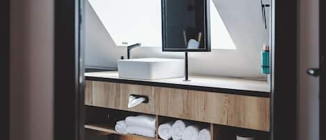 A modern bathroom with a skylight, a sink, and a mirror. There are towels and a trash can visible.