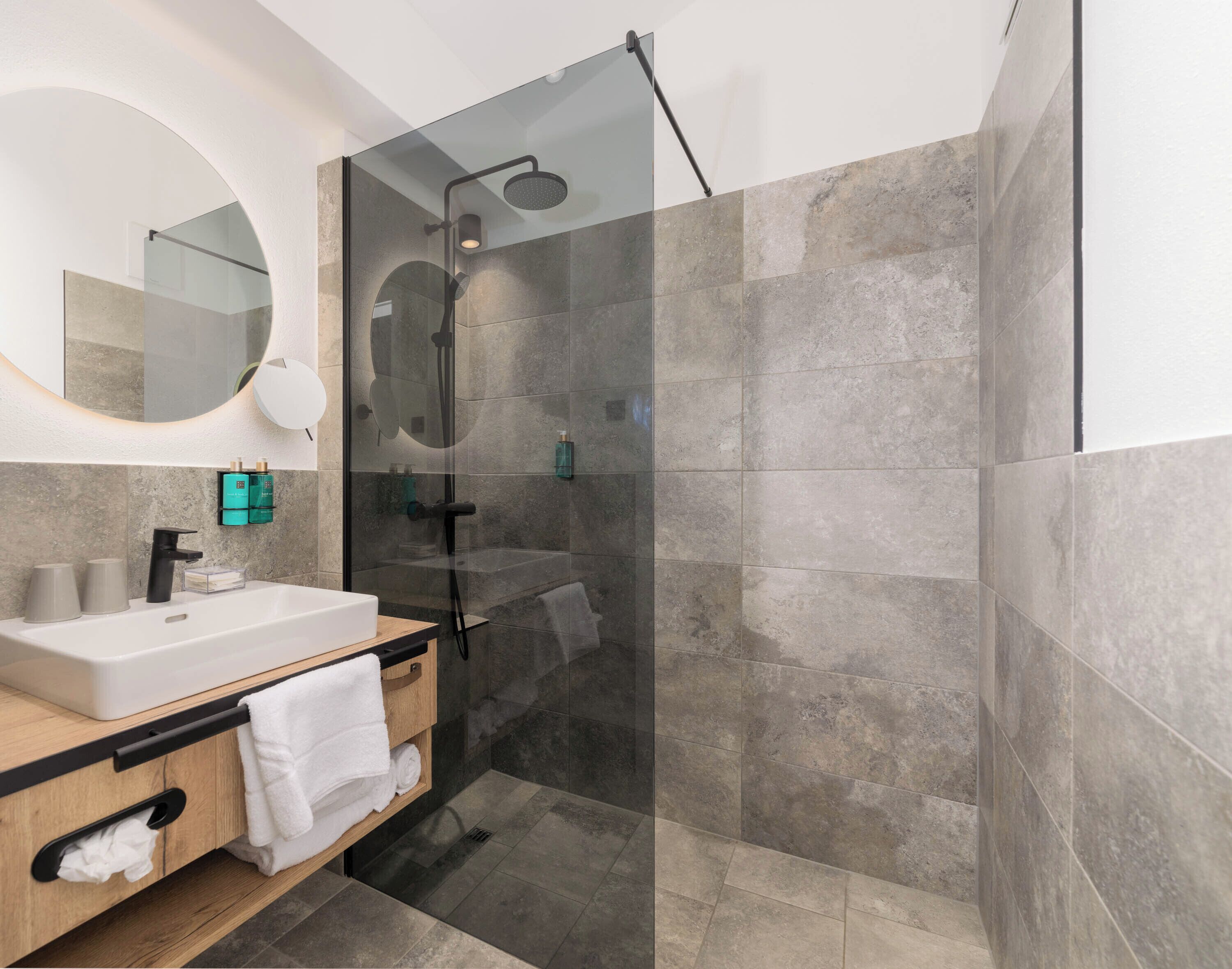 Une salle de bain moderne avec une douche à parois de verre, un meuble-lavabo en bois avec un lavabo blanc et un grand miroir.