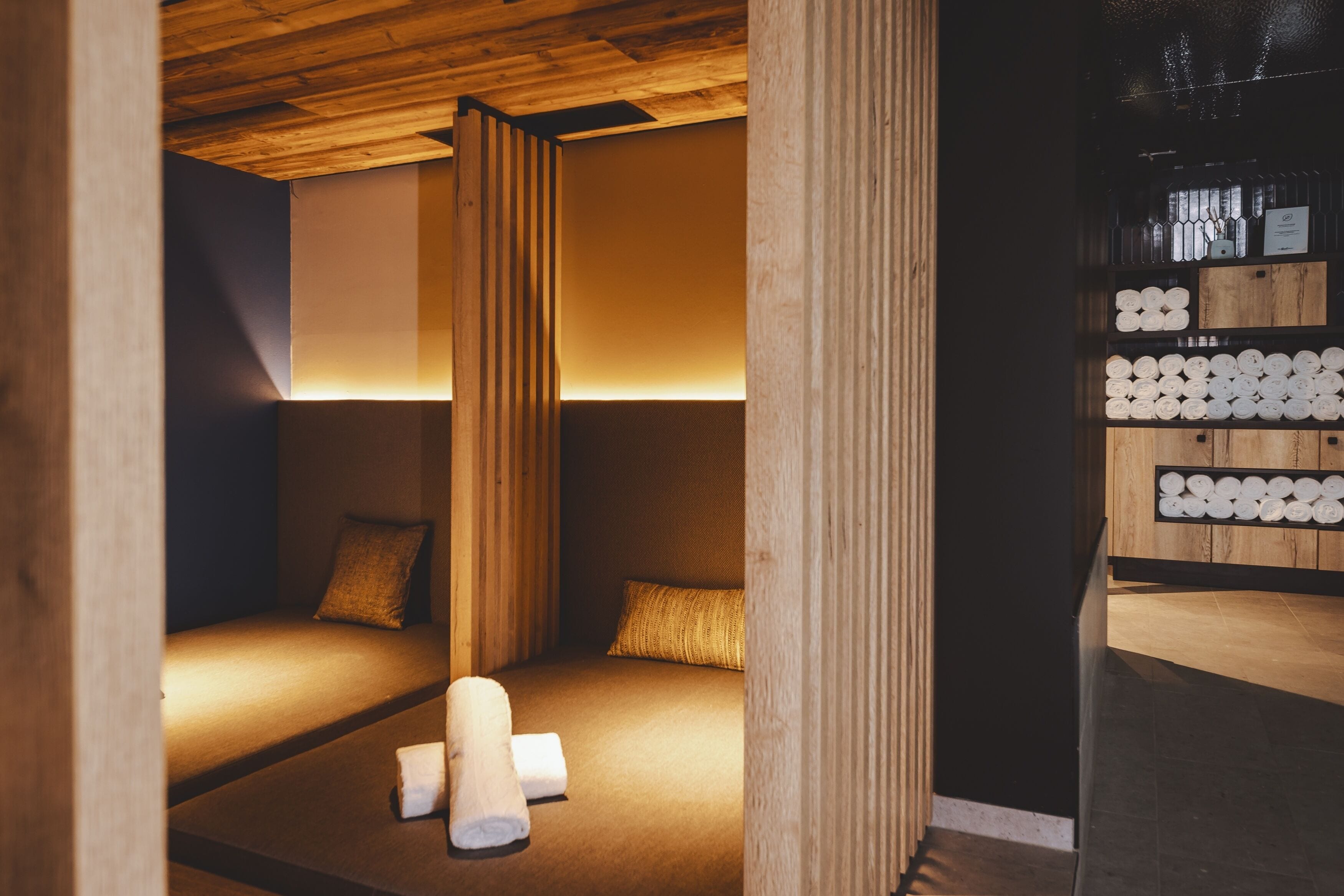 A room with a low wooden ceiling, a bed with a headboard, and a shelf with neatly stacked towels.