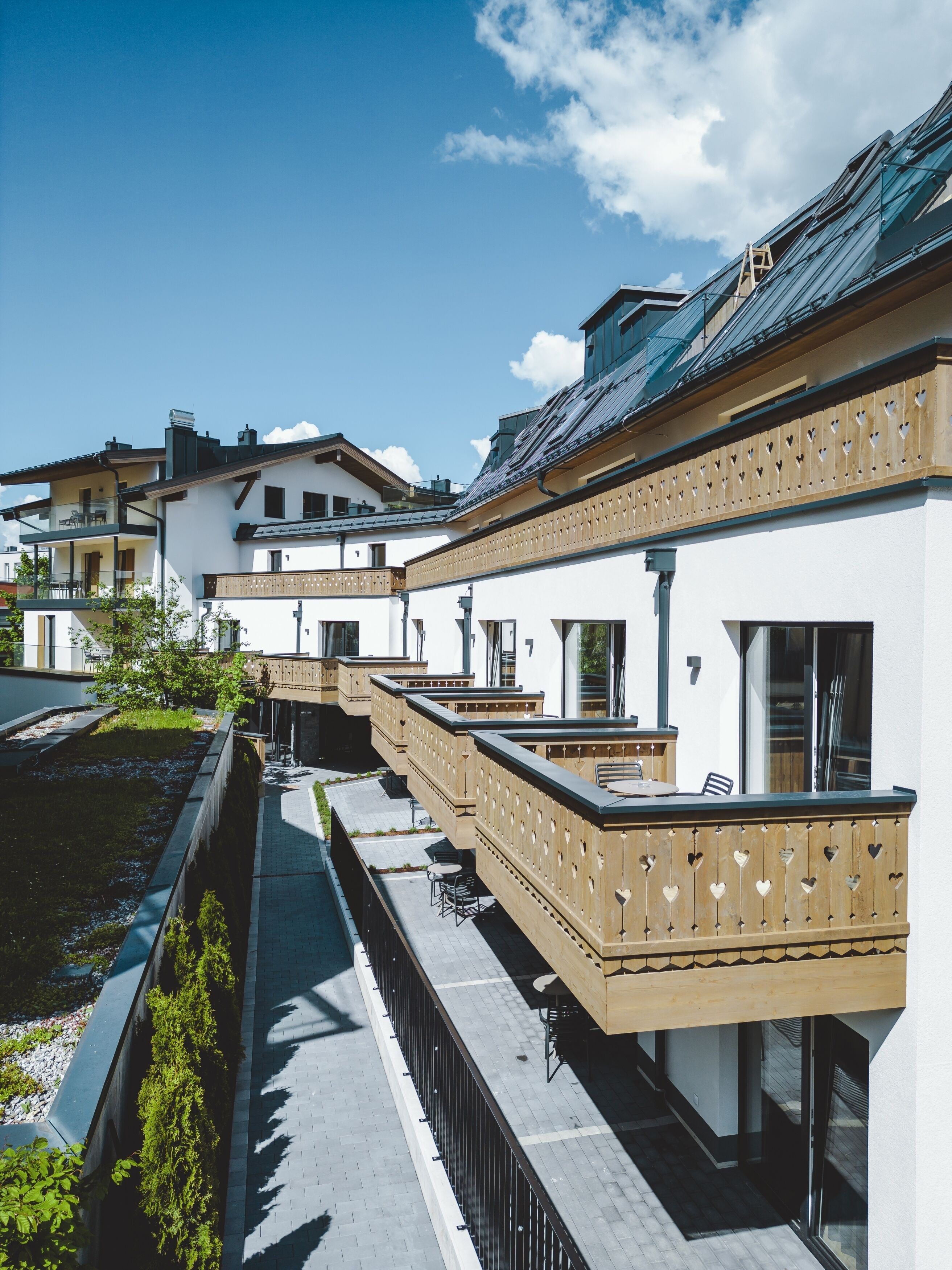 A row of white buildings with balconies, a paved walkway, and a small garden area.
