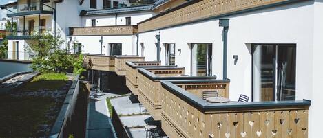 A row of white buildings with balconies, a paved walkway, and a small garden area.