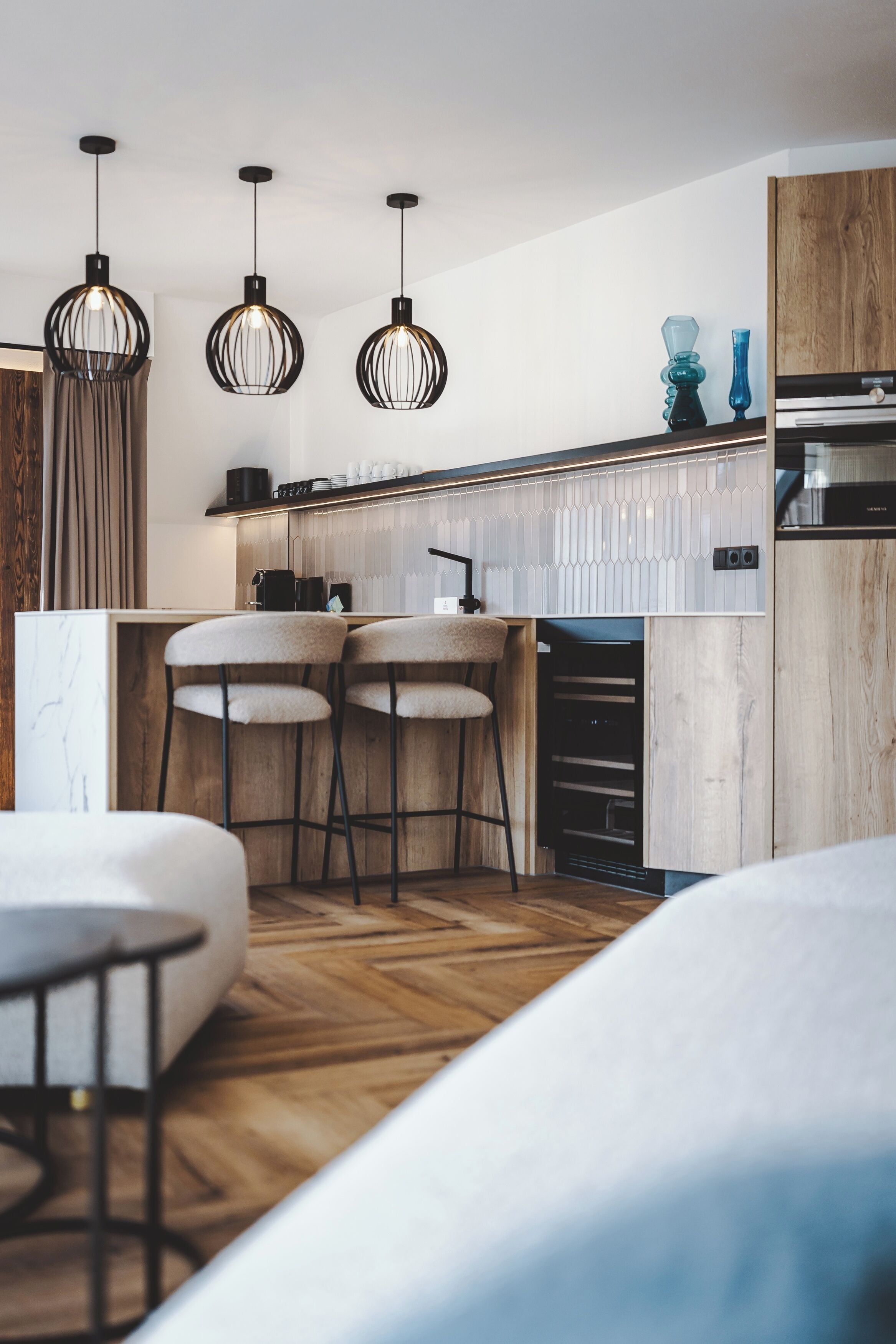 A modern kitchen with pendant lights, bar stools, and a built-in oven.