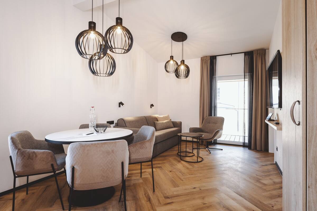Una sala de estar moderna con una mesa de comedor redonda, sofás y sillas. Hay tres lámparas colgantes en el techo.