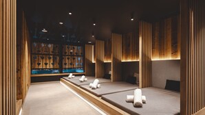 Ein Wellnessraum mit mehreren Massageliegen, Holzvertäfelung und einer Präsentation herzförmiger Massagegeräte.