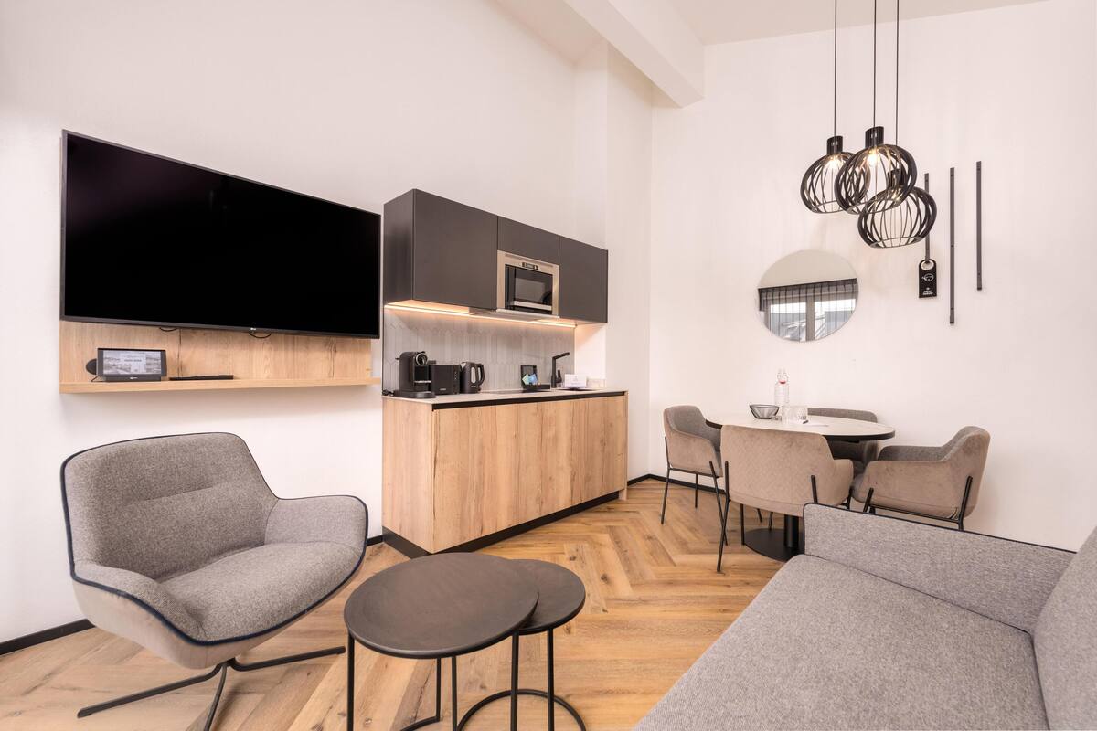 Una cocina moderna con televisión de pantalla plana, armarios de madera y un comedor con mesa y sillas redondas.
