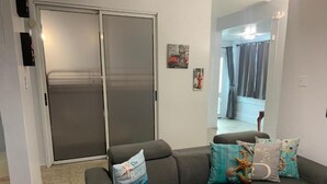 A living room with a grey sofa, a sliding glass door, and a view of a balcony.
