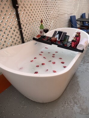 A bathtub with rose petals, a bottle of wine, and toiletries. - Levittown Lakes Suites (Toa Baja)