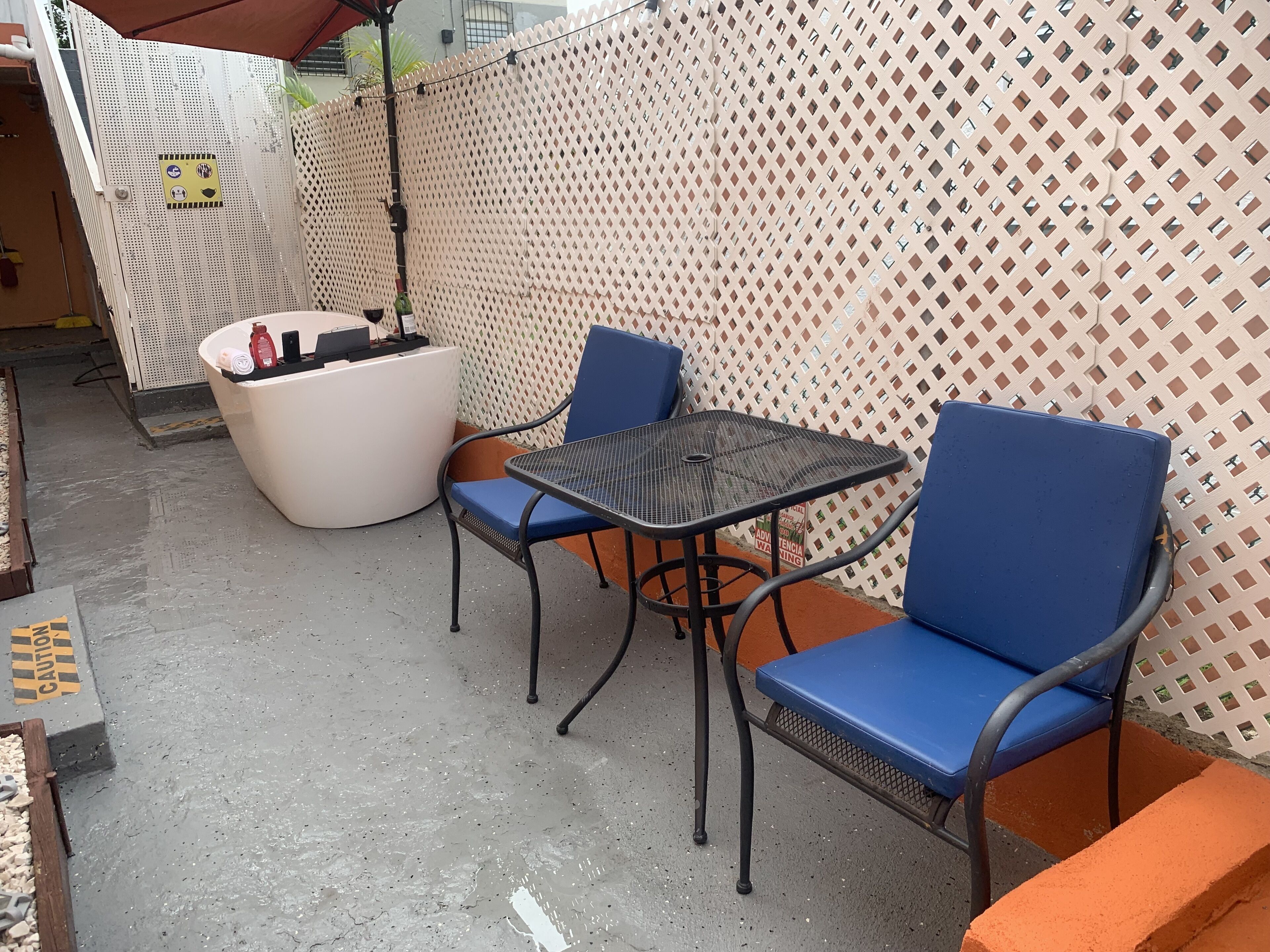 Un patio con una mesa circular para sentarse, dos sillas azules, una maceta blanca y una mesa de metal.