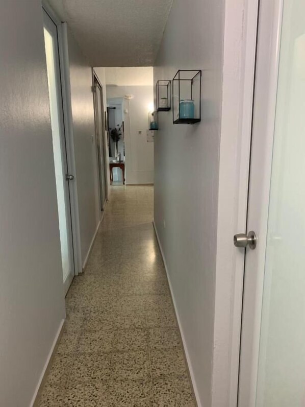 A hallway with a speckled floor, white walls, and a door on the right. - Levittown Lakes Suites (Toa Baja)