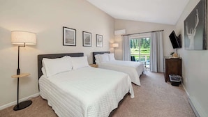 A hotel room with two beds, a standing lamp, a television, and a window with curtains.