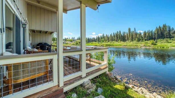 A lakeside cabin with a deck overlooking a calm lake, surrounded by trees.