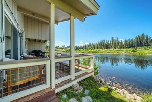 Un chalet au bord du lac, doté d’une terrasse offrant une vue sur un lac paisible, le tout entouré d’arbres.