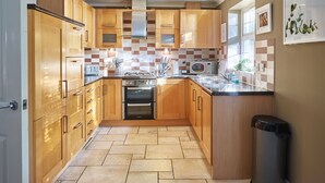 A modern kitchen with wooden cabinets, a gas stove, a microwave, and a sink. - Brookbank Close (Cheltenham)