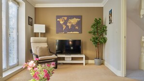 A living room with a beige sofa, a flat-screen TV, a world map on the wall, a potted plant, and a vase with flowers. - Brookbank Close (Cheltenham)