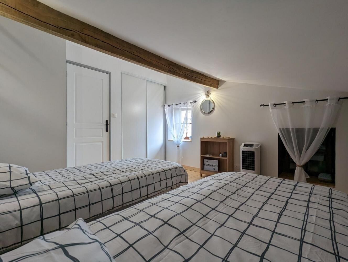 A bedroom with two beds, a wardrobe, a bedside table, a heater, and a window with curtains.