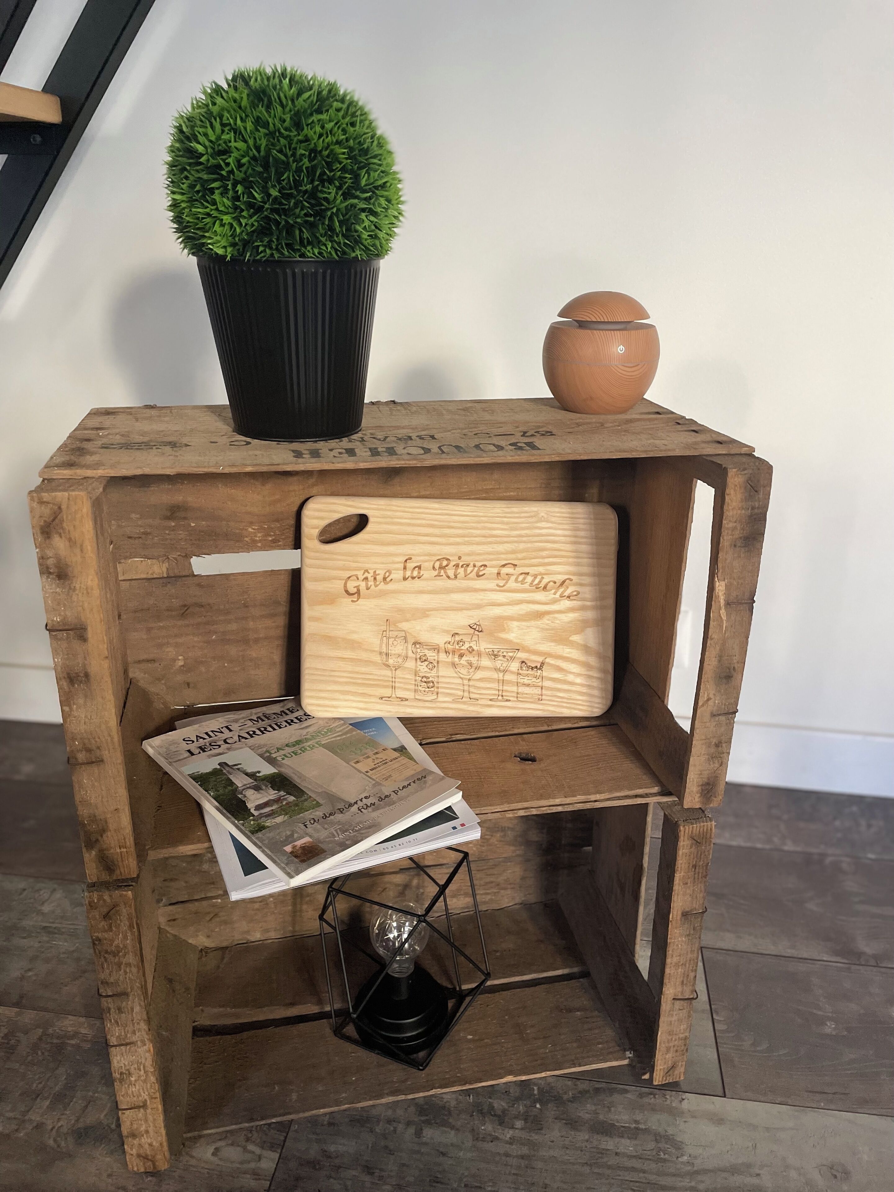 A rustic wooden side table with a potted plant, a clay pot, and a wooden sign with drink illustrations.