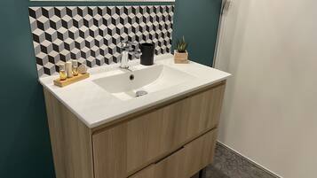 Ein Badezimmer mit einem weißen Waschbecken, einem Holzkosmetikschrank und einer geometrisch gemusterten Rückwand.