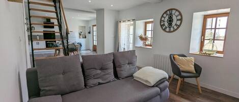 Una sala de estar moderna con un sofá gris, una escalera de madera, un comedor y un gran reloj de pared.