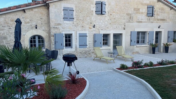 A stone building with a patio area featuring outdoor seating, a grill, and potted plants.