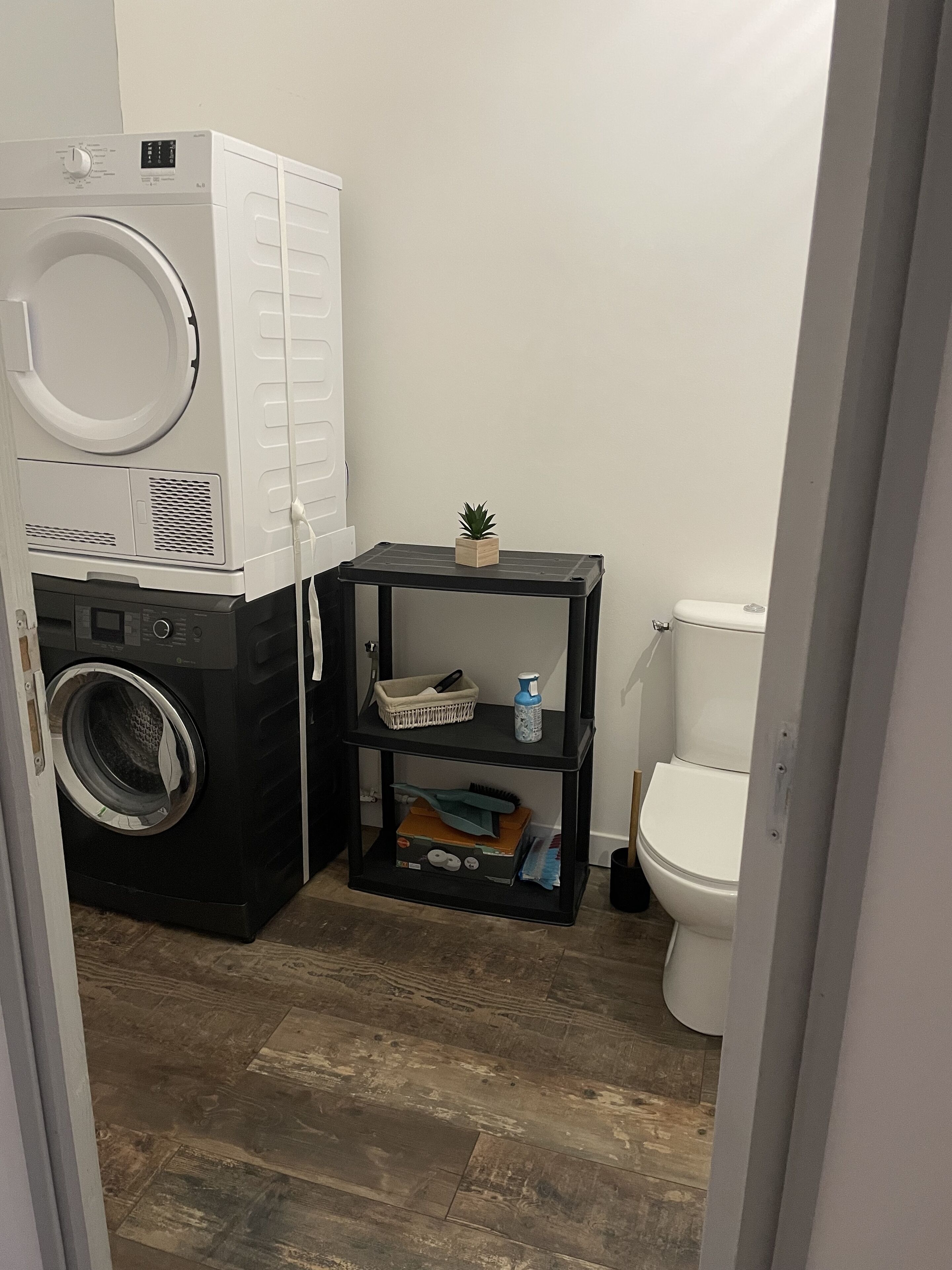 A compact bathroom with a washing machine, a small shelf with toiletries, and a toilet.
