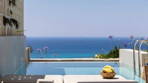 A poolside view with a bowl of bananas, lounge chairs, and a clear view of the ocean. -  Falasarna Luxury Villas (Kissamos)