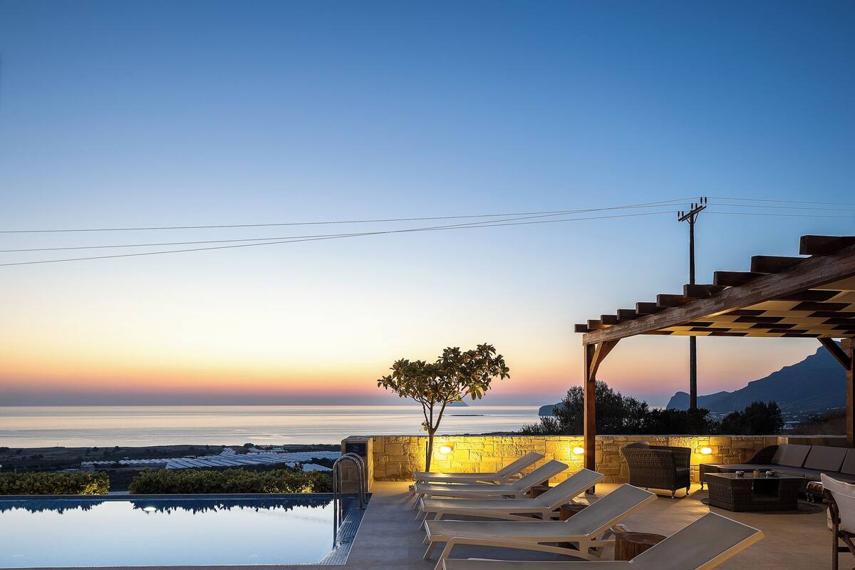 Ein Infinity-Pool mit Liegestühlen und einer Pergola mit Blick auf einen Sonnenuntergang.
