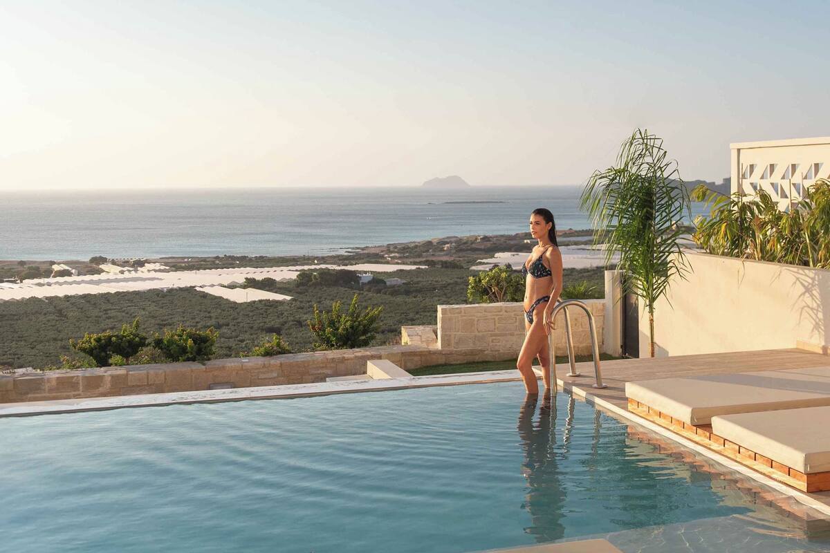 Eine Frau in einem Bikini steht am Pool und blickt auf Strand und Meer.
